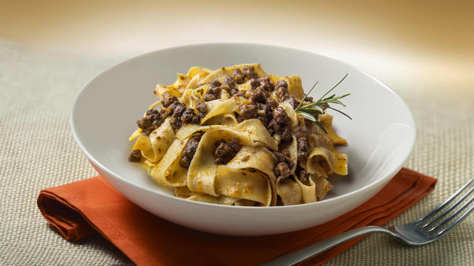 Ciotola bianca con pappardelle al ragù di cinghiale con tovagliolo e forchetta